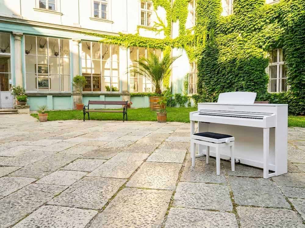 Bílé digitální piano s klavírní stoličkou na nádvoří zámku v Dačicích.